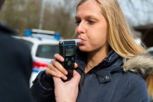 A woman with blonde hair performs a breathalyzer test.